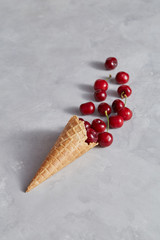 Sweet wafer cone with freshly picked red cherries on a gray background.