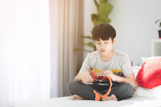 Young asian boy cut the paper for hand craft on bed at home.