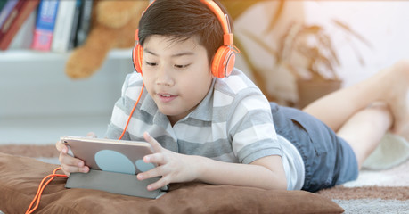 Asian boy lying and Playing Game On Digital Tablet At Home
