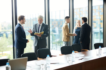 Two small groups of teammates standing in conference hall and preparing with their reports