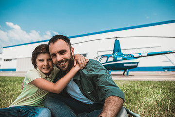 Portrait of satisfied kid embracing positive bearded dad looking at camera while having leisure...
