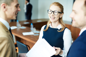Cheerful businesswoman in eyeglasses and formalwear talking to young men and discussing some papers...