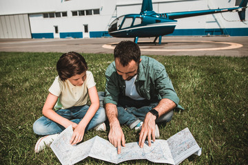 Portrait of smiling boy and outgoing unshaven male having leisure on grass while looking at map...