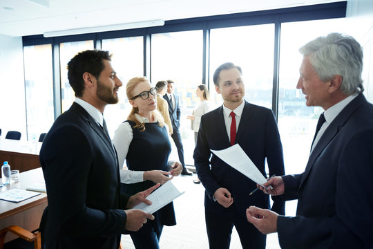 Young and mature politicians in formalwear discussing points of their reports and consulting about ideas