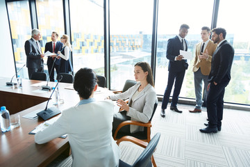 Two young businesswomen and two groups of their colleagues discussing moments of conference with each other