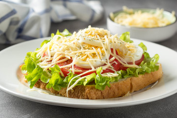 White bread sandwich with lettuce, tomato, boiled egg and grated cheese. Delicious lunch, healthy Breakfast on grey background