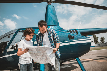 We are here. Portrait of beaming son and outgoing father looking at map while locating near rotor...