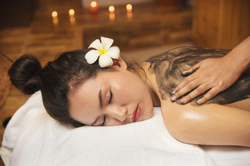Beautiful young woman getting spa massage salon and white flower on her ear.