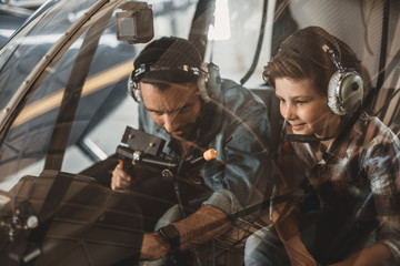 Portrait of happy unshaven man and cheerful son locating in helicopter. Glad dad instructing happy kid