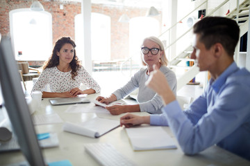 Mature executive sitting at desk with her partners and discussing work during a business meeting