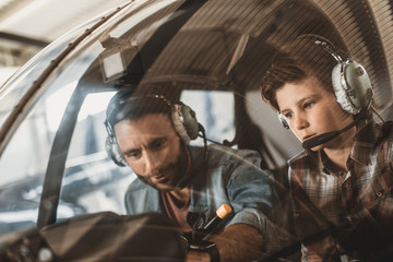 Portrait of concentrated boy and smiling unshaven father adjusting control while wearing headsets. They situating in rotor plane