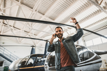 Low angle portrait of bearded cheerful male worker talking on cellphone while gesticulating hands....