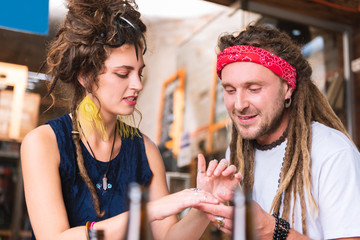Red headband. Hippie man wearing bright red headband looking at his girlfriend hand wearing many...