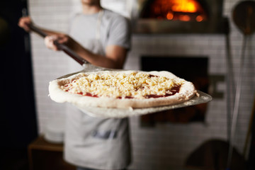 Metallic spade or tray with raw pizza held by baker before putting it into oven
