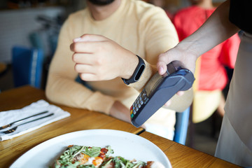 Obraz na płótnie Canvas Contemporary man holding his hand with smartwatch by payment machine while paying for lunch
