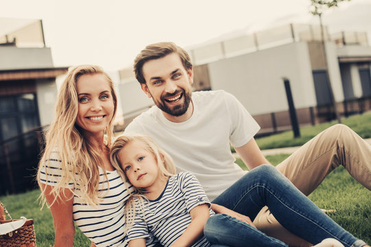 Portrait of cheerful bearded husband locating near outgoing wife and smiling kid. They looking at camera outdoor. Positive family relaxing in open air concept