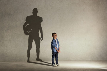 American Football champion. Childhood and dream concept. Conceptual image with boy and shadow of fit athlete on the studio wall