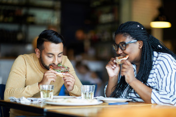 Hungry girl and guy eating appetizing pizza with bacon in cafe or restaurant by lunch