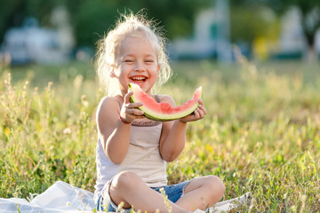 Little blond girl eating watermelon in the park.