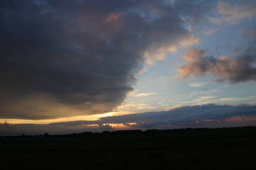 Dark clouds with several sunbeams during sunset in colorful sky in the Netherlands.