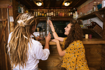 Putting glasses. Two young creative beaming owners of pub having fun while putting glasses on bar stand