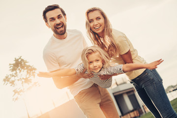 Portrait of happy unshaven husband and beaming wife keeping positive little girl in hands. Pleased...