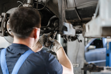 Car mechanic inspecting car wheel and repair suspension detail. Lifted automobile at repair service station. replacement of ferrule and leverage