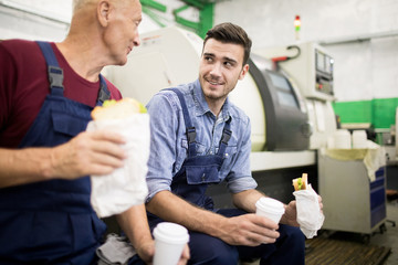Two operators sitting and eating sandwich and drinking coffee during lunch in factory