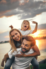 Portrait of happy unshaven husband spending tie with cheerful wife and satisfied female child in...