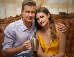 Young couple portrait at vintage stile pub bar restaurant holding cocktail drink.