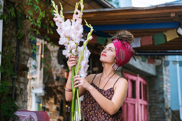 Looking at flowers. Dark-haired woman wearing red headband feeling cheerful while looking at flowers