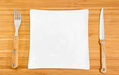 Empty square white dish, fork and knife with wooden handles