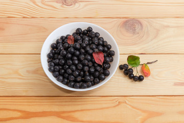 Chokeberry in bowl and berries cluster on a wooden surface