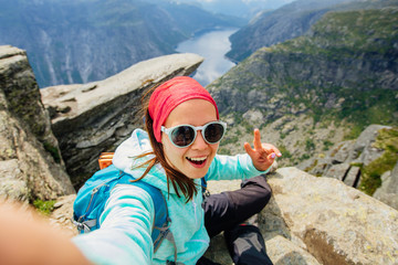 Sportive smiling woman hiker in eyeglasses making selfie portrait above Trolltunga and Norwegian...