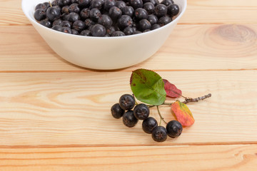 Chokeberry branch against of bowl with berries on wooden surface
