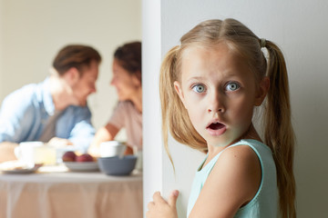 Obraz na płótnie Canvas Surprised little girl heard breaking news during her parents talk by breakfast in the kitchen