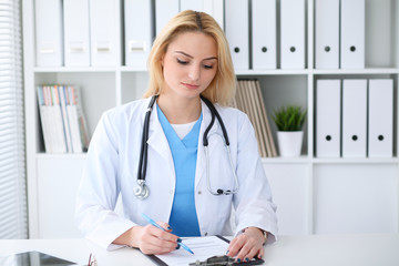 Doctor woman at work. Portrait of cheerful smiling blonde physician sitting at the desk. Medicine and healthcare concept