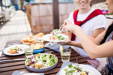 Young man offering salad or appetizer to his girlfriend during their lunch in outdoor cafe