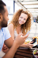 Young woman and her boyfriend with smartphones sitting by served table in outdoor cafe and discussing curious vids