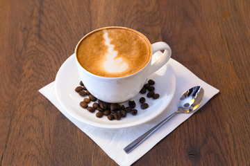 Closeup of a cup of coffee with beans and a spoon on dark wooden table