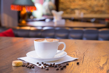 Fototapeta premium Closeup of a cup of coffee with beans and a cookie on wooden table, blurred background