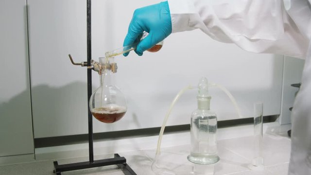 backside view lab assistant pours brown liquid into flask