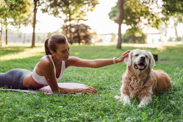  Exercising with friend. Young beautiful fit woman in sportswear exercising with the dog while...
