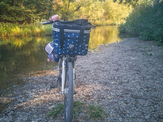Buntes Fahrrad steht am Flussufer. Ein Damenfahrrad mit blauem Dekorationen parkt auf Kieselsteinen...