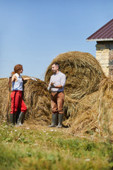 Naklejka na ściany i meble Young contemporary farmers with worktools standing by hay stack and discussing work