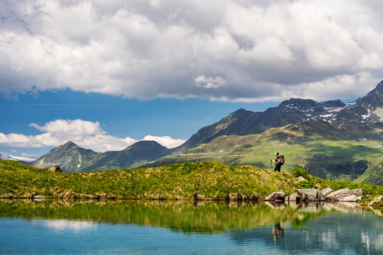 Female traveler with backpack hiking mountain trail next to a mountain lake and admiring views of Swiss Alps in Val de Bagnes area, Switzerland.