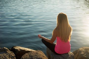 Fototapeta na wymiar Yoga at dawn by the sea, on large stones. Girl with long blond hair, slim build. Relax and meditation by the water. Meeting a new day