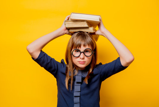 Portrait of a nerd girl in glasses with books on yellow background