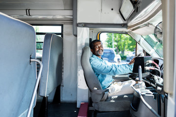 mature african american driver sitting at bus and looking at camera