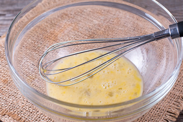 Wire whisk and brown eggs in a glass bowl